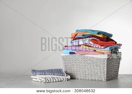 Wicker Laundry Basket With Clean Clothes On Table Against Light Background. Space For Text