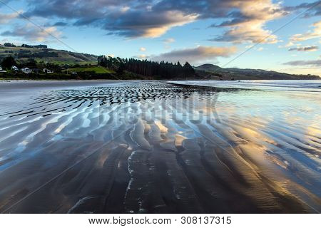 Gentle cloud colors are reflected in the ocean water. Low tide. Strips of sand and water left by the ocean tide. The art of artistic photography. New Zealand, Pacific Coast The concept of tourism
