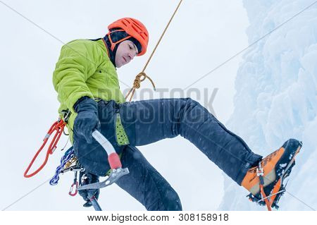 Alpinist Man With Ice Tools Axe In Orange Helmet Climbing A Large Wall Of Ice. Outdoor Sports Portra