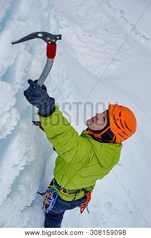Alpinist Man With Ice Tools Axe In Orange Helmet Climbing A Lar