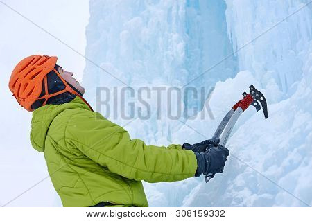 Alpinist Man With Ice Tools Axe In Orange Helmet Climbing A Lar