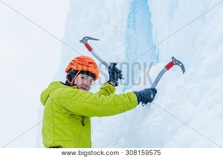 Ice Climber Man With Ice Tools Axe In Orange Helmet Climbing A Large Wall Of Ice. Outdoor Sports Por