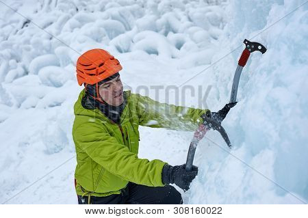 Alpinist Man With Ice Tools Axe In Orange Helmet Climbing A Large Wall Of Ice. Outdoor Sports Portra