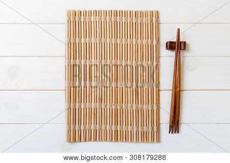 Two Sushi Chopsticks With Empty Bamboo Mat Or Wood Plate On Wooden Background Top View With Copy Sta