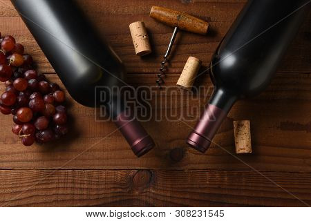 Wine Still Life: Two Cabernet Sauvignon wine bottle short from directly above on a dark wood table with grapes corks and cork screw and copy space.