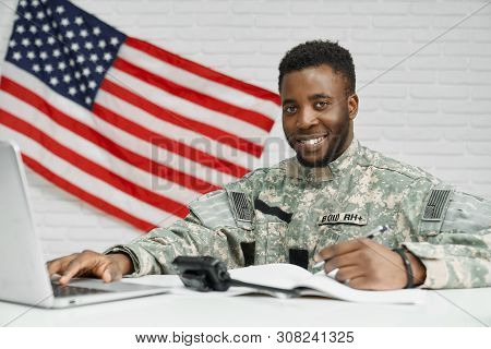 Positivity Soldier And Worker Of American Army Writing Documents, Using Laptop And Smiling At Camera