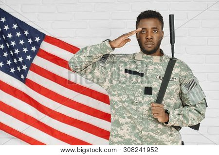 Young Serious Ranker Standing Near American Flag And Holding Hand Near Head, Ready For Army. Soldier