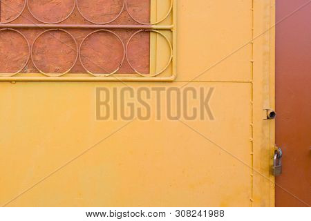 Yellow Wall With Trellised Battened Window And Metal Door Closed With Padlock. Round Elements Of Rac