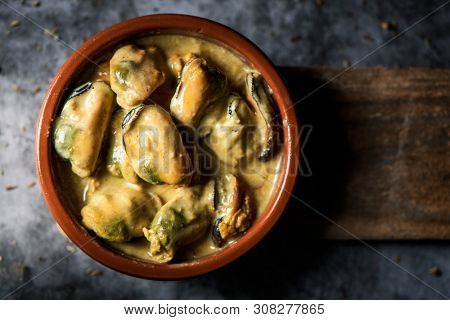 high angle view of an earthenware plate with mejillones al curry, spanish curried mussels, on a stone surface