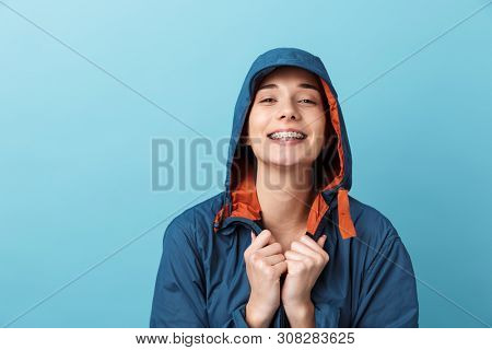 Cheerful young girl wearing raincoat standing isolated over blue background, posing