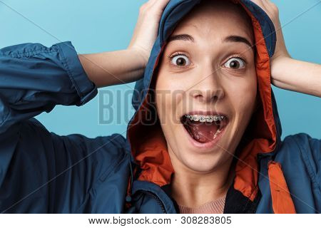 Cheerful young girl wearing raincoat standing isolated over blue background, posing, screaming