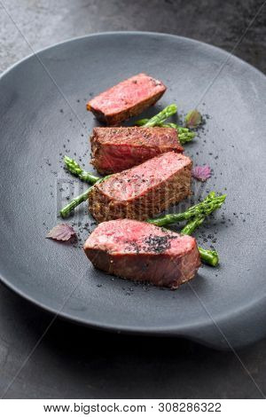 Barbecue dry aged wagyu fillet steak with blanched green asparagus tips and herbs as closeup on a modern design plate with copy space
