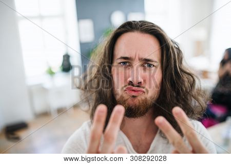 A Portrait Of Young Man With Long Hair Indoors, Fingers Forming V For Victory.