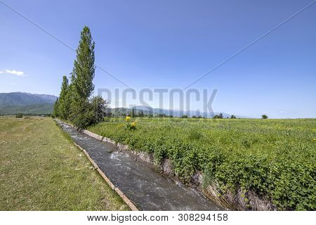 View Of The Central Tien Shan Mountains In Kyrgyzstan With Flowing Water In The Aryk And Green Field