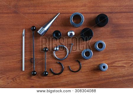 Jewelry Piercing Set. Piercing Accessories On Wooden Background. Stretching For Ear Tunnels , A Cath