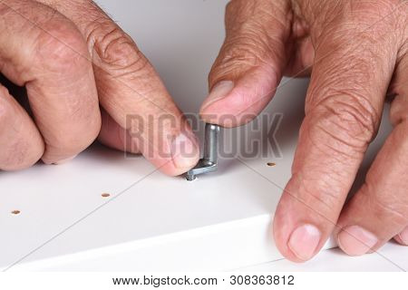 Closeup of a man assembling a DIY piece of furniture. The person is inserting a shelf support pin into a pre-drilled hole.