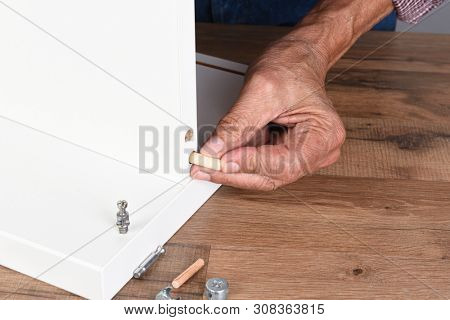 Closeup of a man assembling a DIY piece of furniture. The man is inserting a wooden dowel into a pre-drilled hole.