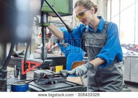 Metal worker woman operating drilling machine concentrating on her job