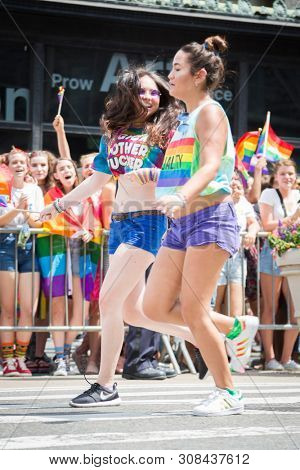 2018 JUNE 24 NEW YORK: Two NYC Pride March participants wearing rainbow colored tshirts run together holding hands past cheering spectators on the 5th Ave parade route.