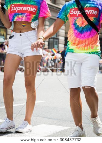 2018 JUNE 24 NEW YORK: Two NYC Pride March participants walk together holding hands wearing rainbow colored tshirts on the 5th Ave parade route.