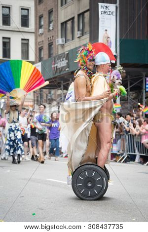 2018 JUNE 24 NEW YORK: Two NYC Pride March participants dressed in Roman gladiator outfits ride on a segway along the 5th Ave parade route.