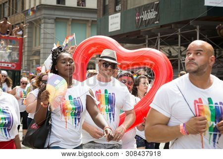 2018 JUNE 24 NEW YORK: NYC Pride March participants wearing PVH tshirts walk along the 5th Ave parade route with a red heart balloon. Phillips-Van Heusen Corporation is an American clothing company.