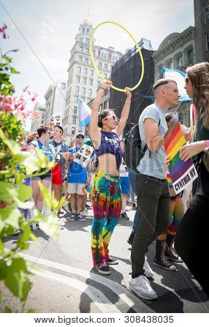 2018 JUNE 24 NEW YORK: NYC Pride March participant wearing a rainbow outfit raises a hulahoop while walking along the 5th Ave parade route.