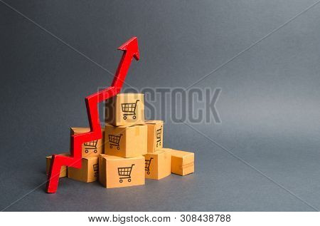 A Pile Of Cardboard Boxes With Drawing Of Shopping Carts And A Red Up Arrow. The Growth Rate Of Prod