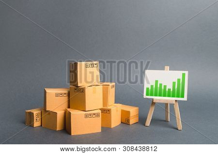 Pile Of Cardboard Boxes And A Stand With Information Chart. Rate Growth Of Production Of Goods And P