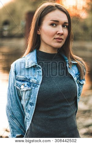 Portrait Of The Attractive, Slender, Beautiful Young Caucasian Blonde Girl In A Jeans Jacket. Smilin