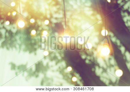 Blurred Bokeh Light On Sunset With Yellow String Lights Decor In Tree
