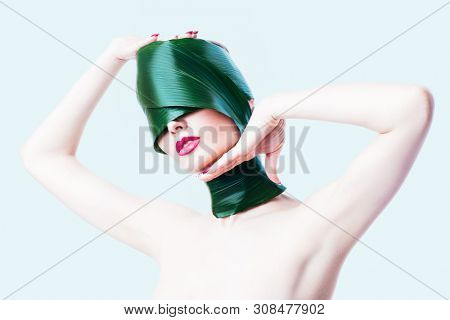 A close up portrait of a beautiful girl with a head rolled up in a leave posing in the studio over the white background. Beauty, nature, make up.