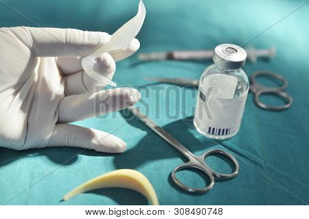 Hand Holding Silicone Nasal Implant In Operating Room With Surgical Equipment And Medicine Vial Back