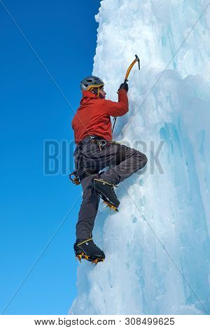 Alpinist Man With Ice Tools Axe Climbing A Large Wall Of Ice. Outdoor Sports Portrait.