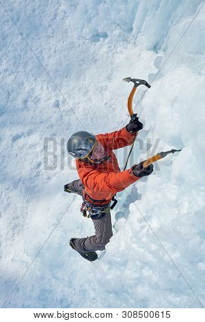 Alpinist Man With Ice Tools Axe Climbing A Large Wall Of Ice. Outdoor Sports Portrait.