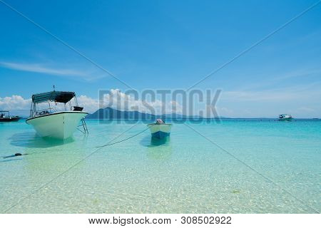 White Coral Sand Beach  With Moored Line-up Of Boats Used To Bring Tourists To Island Surrounded By 
