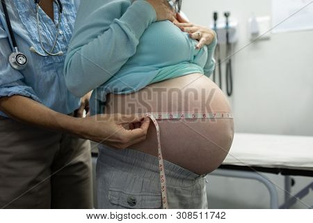 Mid section of Caucasian female doctor measuring pregnant woman belly in examination room at hospital