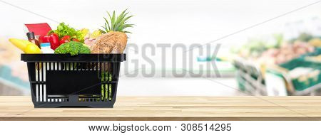 Food And Groceries In Shopping Basket On Wood Table With Blurred Suppermarket In Background, Panoram