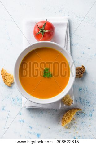 A warm and delicious bowl of tomato soup with crotons. Top view of healthy vegetarian soup shot from above on grunge white background with scattered bread crotons and a fresh tomato.