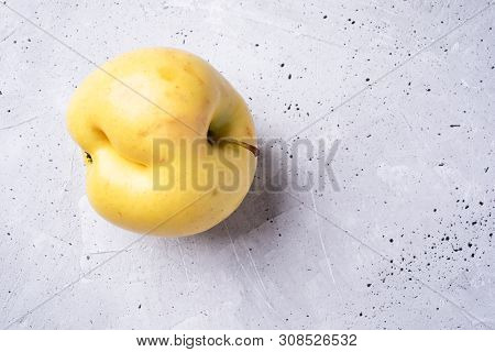 One Ugly Yellow Apple On Grey Concrete Background.