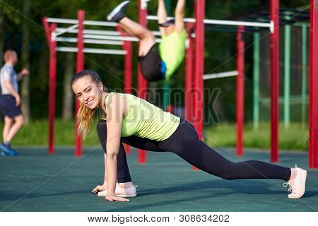 Happy Young Woman Stretching Before Running Outdoors In Workout Sports Ground