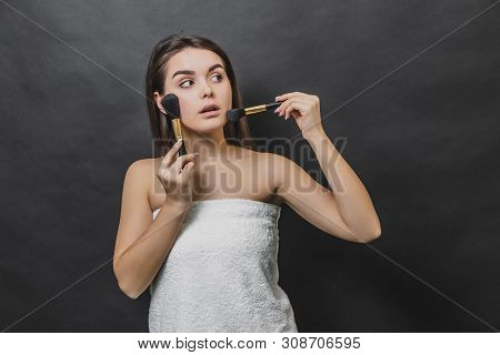 Thoughtful Gorgeous Girl In White Towel Holding Two Makeup Brushes. She Is Looking Up And Leftwards.