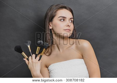 Beauty Caucasian Girl In White Towel Holds Makeup Brushes. She Is Looking Leftwards.