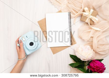 Female Hand Holding Modern Camera On A Wooden Background With Peonies Flowers. Top View, Tender Mini