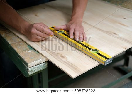 Carpenter Marking Straight Line On Plywood Sheet Using Spirit Level In Carpentry Workshop. Measuring