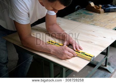 Carpenter Marking Straight Line On Plywood Sheet Using Spirit Level In Carpentry Workshop. Measuring