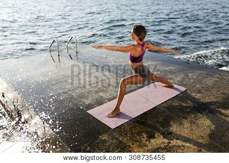 Smiling Woman Pulling Hands Aside While Training Yoga Poses By The Sea