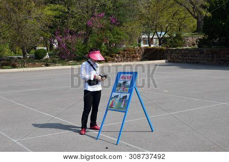 Pyongyang, North Korea - May 1, 2019: Girl Street Photographer Offers To Make A Photo In The Taesong