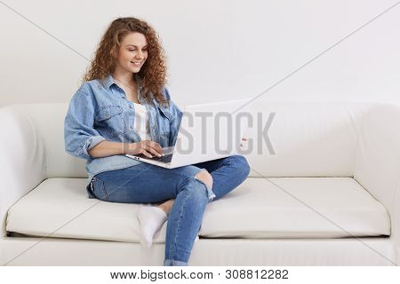 Horizontal Shot Of Nice Looking Lovely Attractive Woman, Focused Curly Haired Girl Sitting On White 