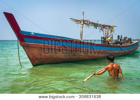 A Fisherman Wades Out In Waist Deep Water To His Colourful Wooden Boat Off The Beach At Ngapali, Mya